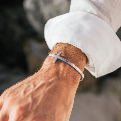 Cross bracelet worn on wrist with polished cuff band and raised cross detail