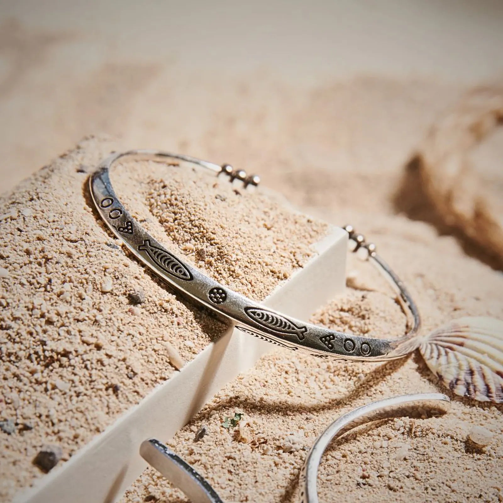 Cuff Bracelet displayed in sand with shells, showing engraved fish pattern and open cuff shape
