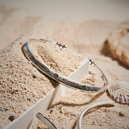 Cuff Bracelet displayed in sand with shells, showing engraved fish pattern and open cuff shape