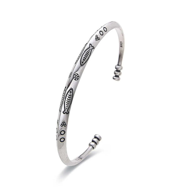 Cuff Bracelet shown in angled profile with fish engravings, dotted symbols, and rounded ends