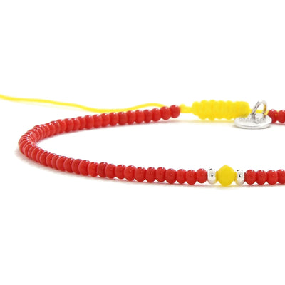 Close-up of Man Bracelet Beads showing red seed beads with yellow accent beads, silver charm, and cord closure