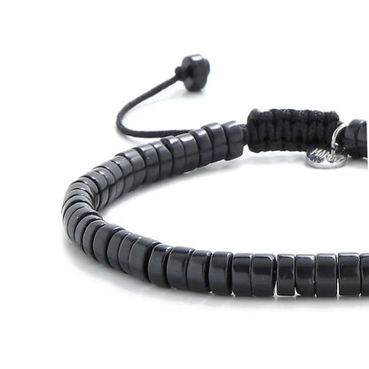 Close-up of matte black bracelet showing matte black clay beads with silver charm, silver charm, and cord closure