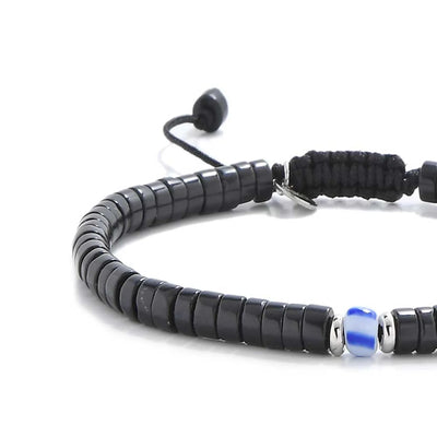 Close-up of Mens Black Pearl Bracelet showing matte black clay beads with blue accent bead, silver charm, and cord closure