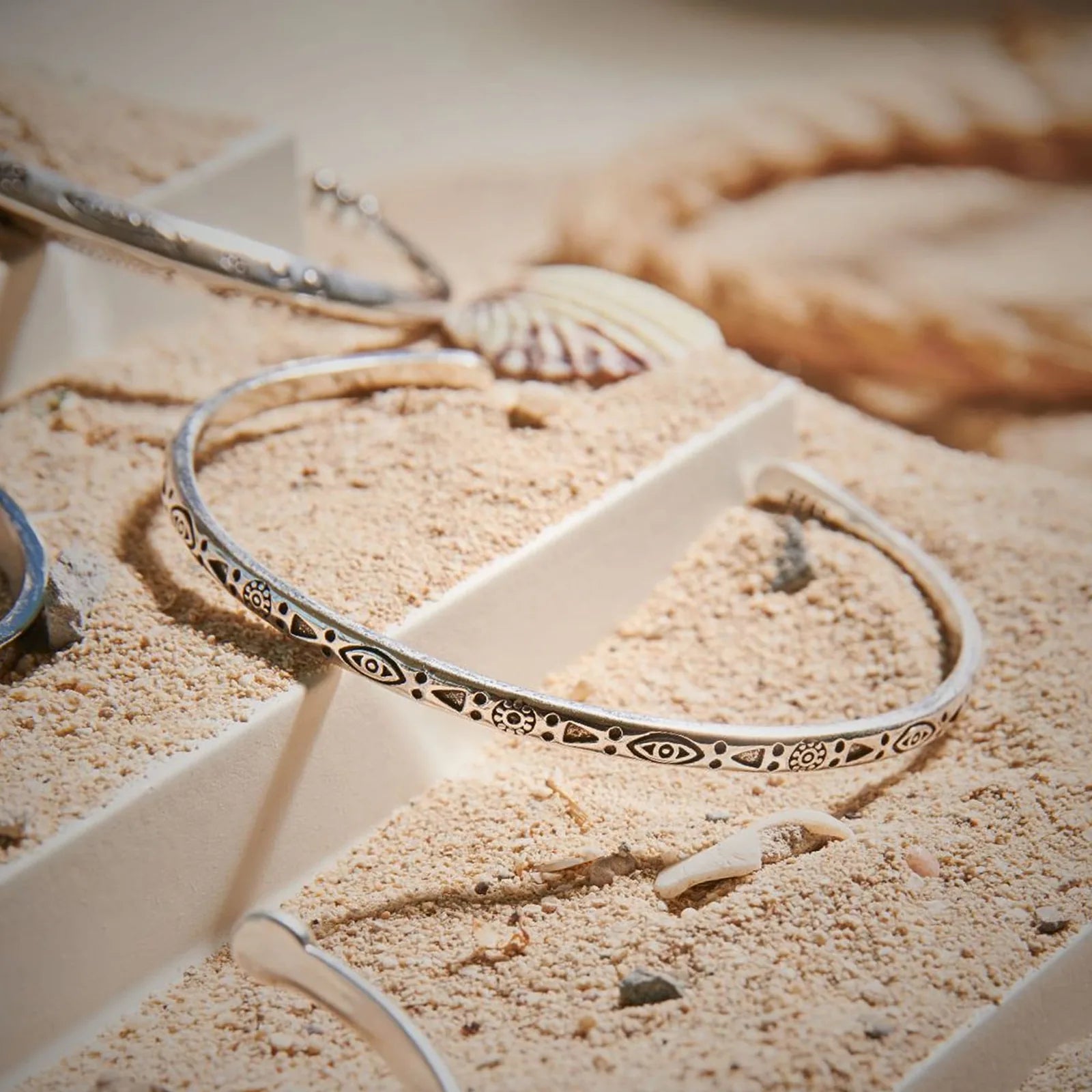 Mens Stainless Steel Bracelets displayed in sand with shells, showing patterned open cuff design