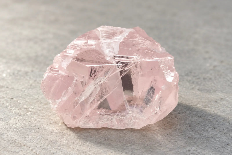 Pale pink diamond specimen with angular surfaces and visible internal fractures.
