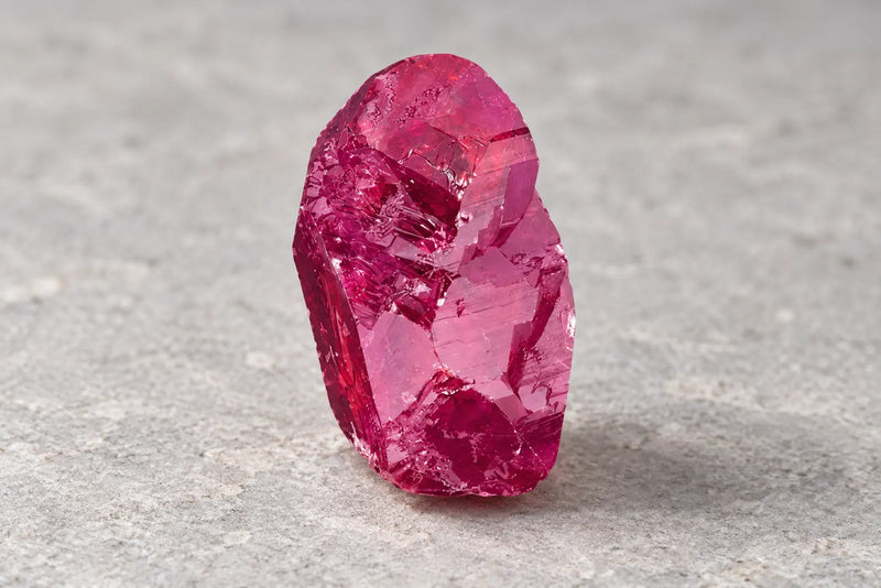 Deep pink sapphire crystal with uneven edges and visible internal lines.