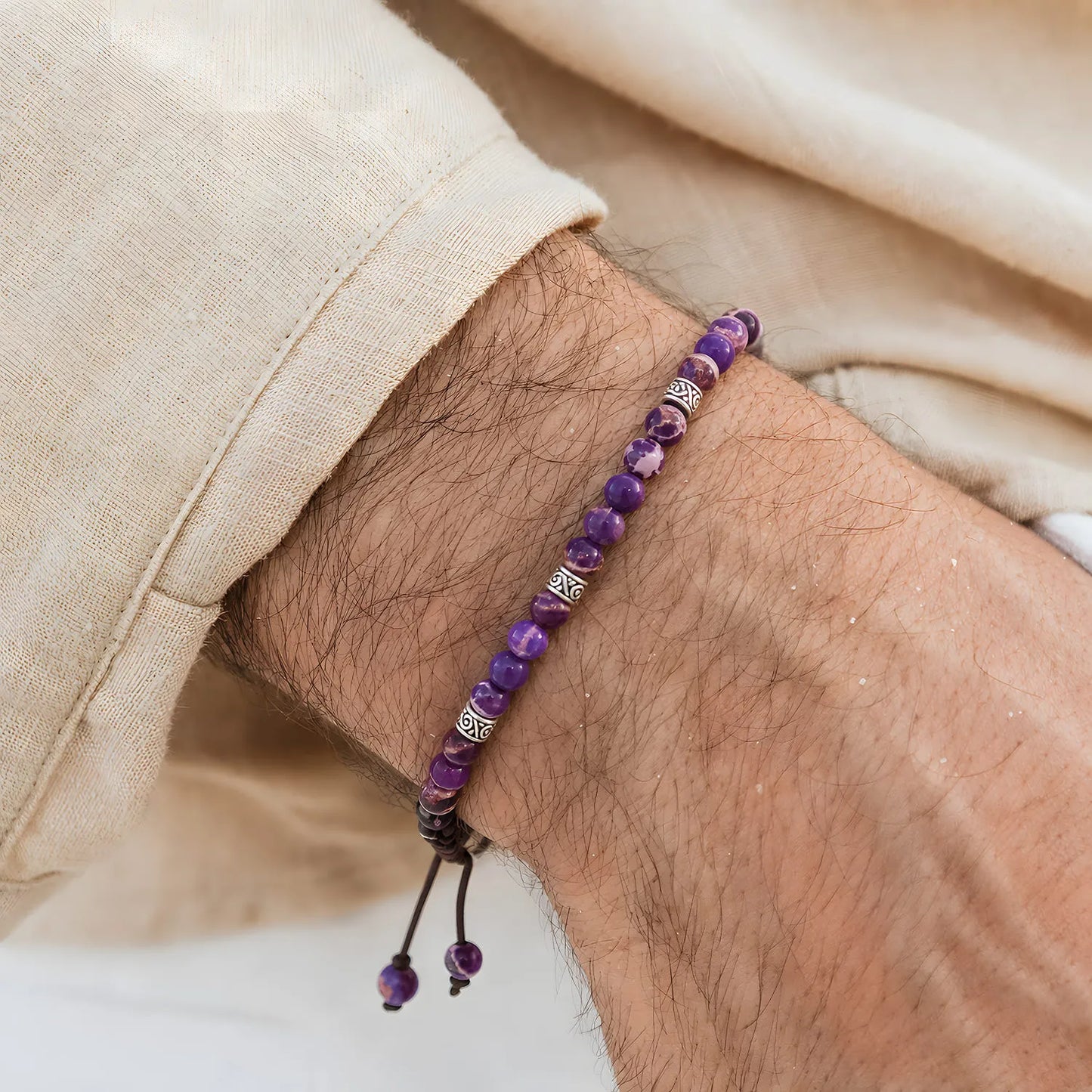 Purple Jasper Bracelet worn on a wrist with silver spacer beads, brown cord, and cream fabric sleeve.