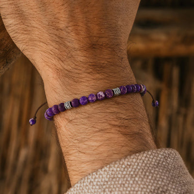 Purple Jasper Bracelet on a wrist with silver spacer beads and brown cord against a warm wood background.