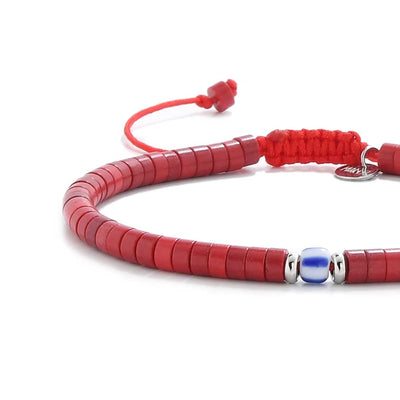 Close-up of red gemstone jewelry showing red clay beads with blue accent bead, silver charm, and cord closure