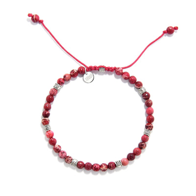 Top view of Red Jasper Bracelet with round red beads, silver spacers, red cord, and small charm.