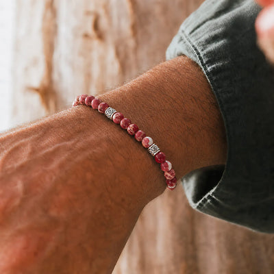 Red Jasper Bracelet worn on a wrist with silver spacer beads and red cord against a warm wood background.