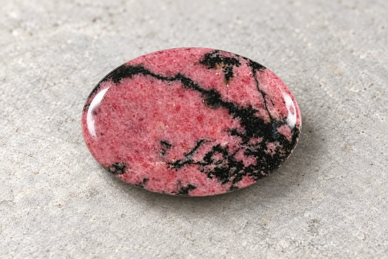 Polished oval rhodonite with a pink surface crossed by dark veins and patches.