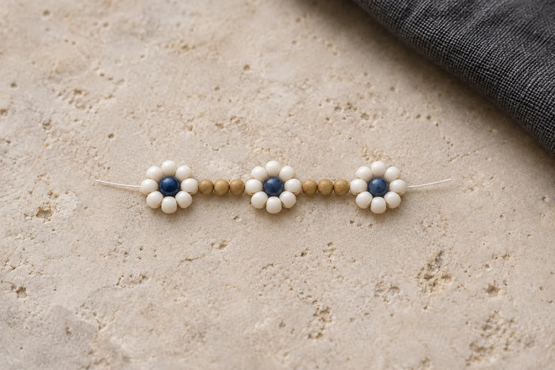 Three off-white eight-petal flowers with blue centers and three sandy beige spacer beads between each flower.