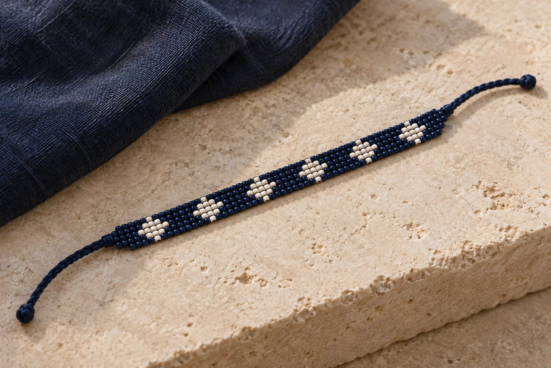 Narrow navy and off-white diamond seed bead loom band with one braided thread tie at each end.