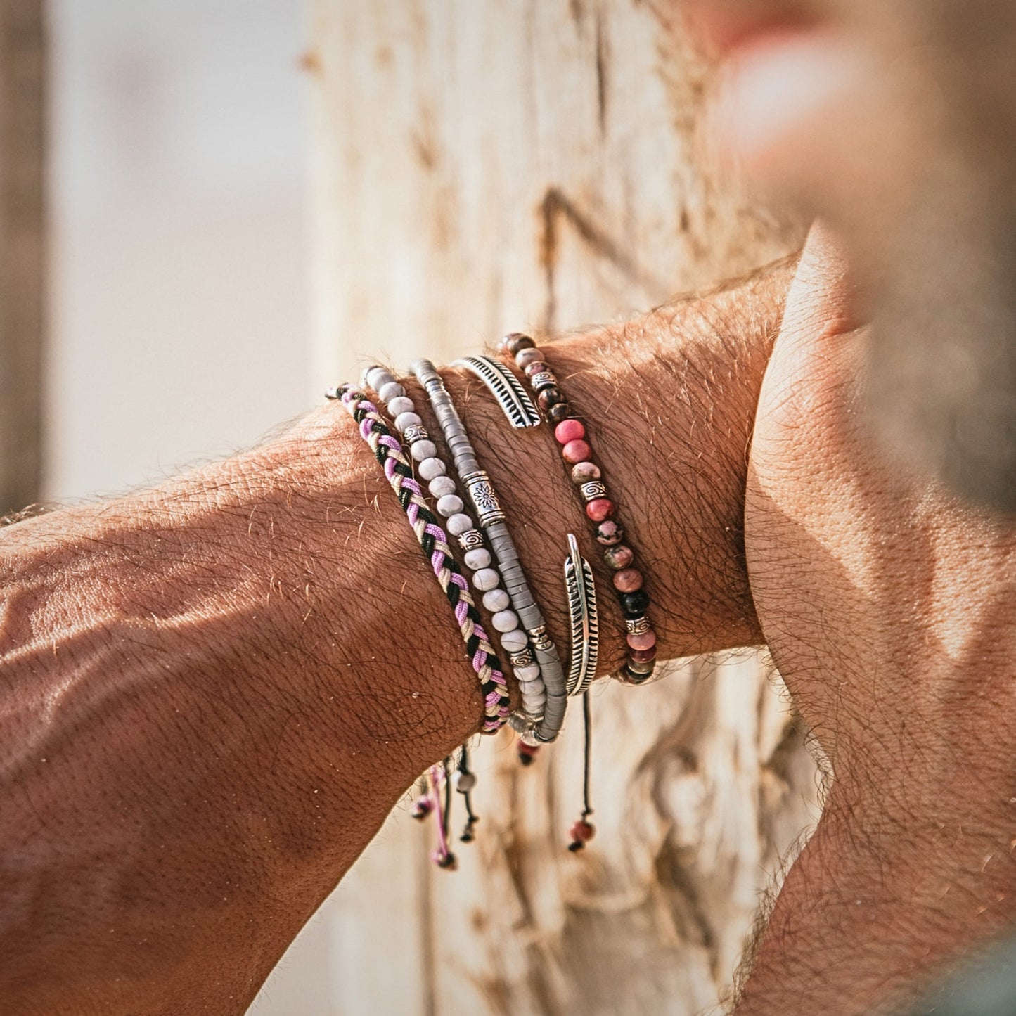 Man wearing shamballa bracelet stack with gray and beaded designs against sunlit background