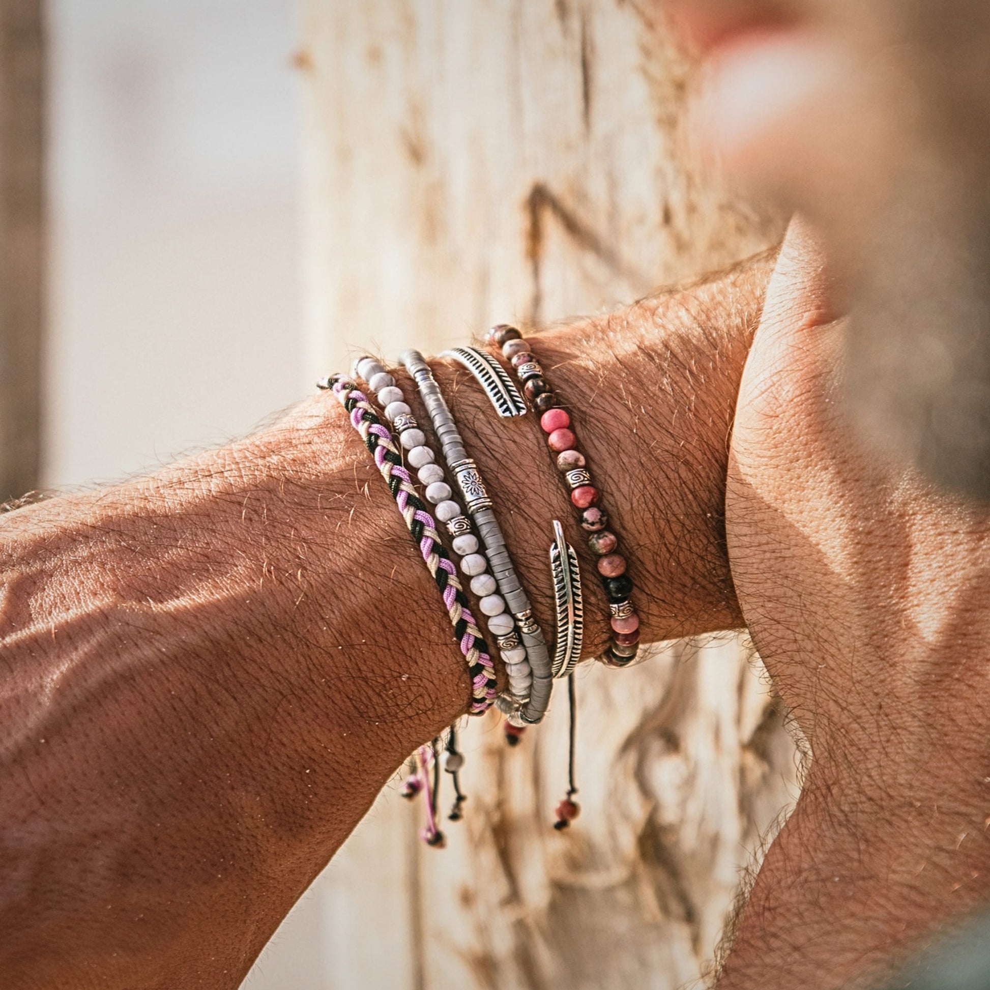 Man wearing shamballa bracelet stack with gray and beaded designs against sunlit background