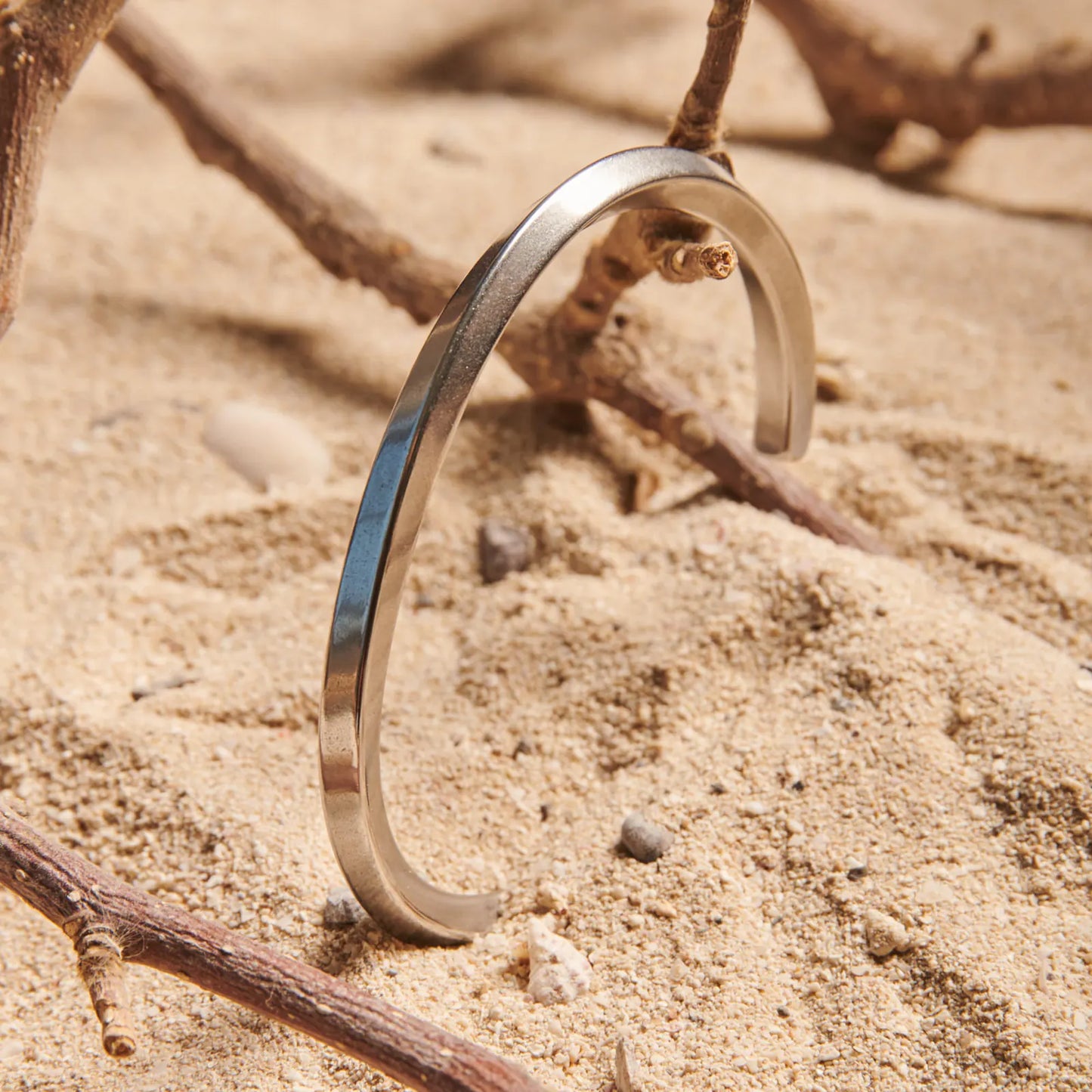 Stainless steel bracelet for men standing in sand, showing plain polished cuff design