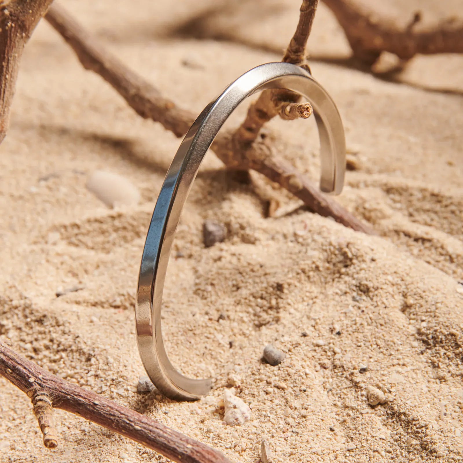 Stainless steel bracelet for men standing in sand, showing plain polished cuff design