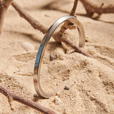 Stainless steel bracelet for men standing in sand, showing plain polished cuff design