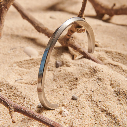 Stainless steel bracelet for men standing in sand, showing plain polished cuff design