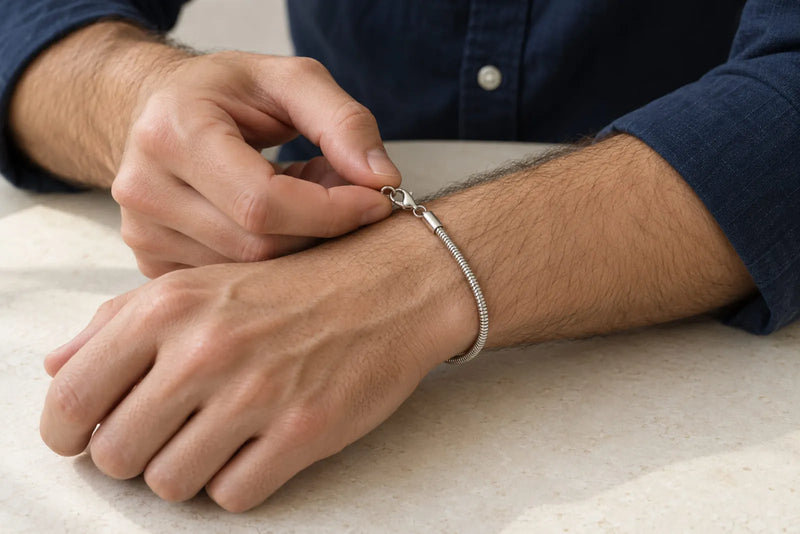 Types of bracelet clasps in use: a man fastening a silver-tone snake-chain bracelet at his wrist.