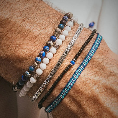 White Jade Bracelet stacked on a wrist with blue beads, silver cuff, black beads, and woven cord.