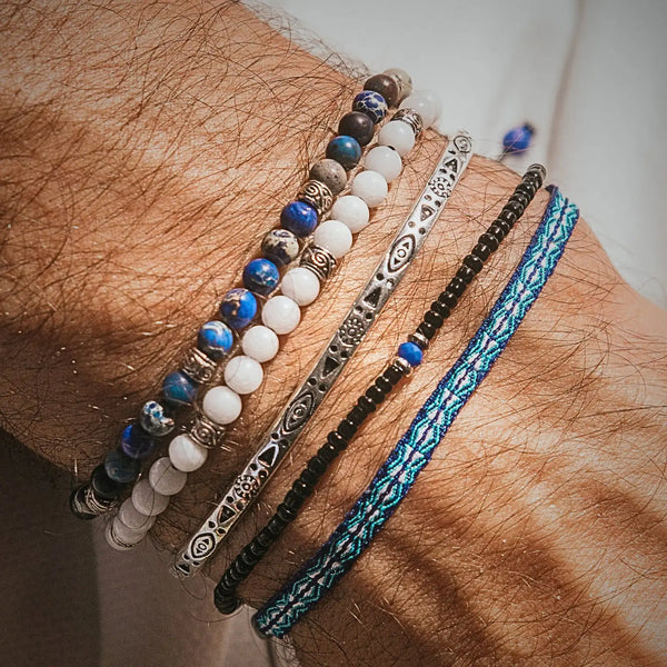 White Jade Bracelet stacked on a wrist with blue beads, silver cuff, black beads, and woven cord.