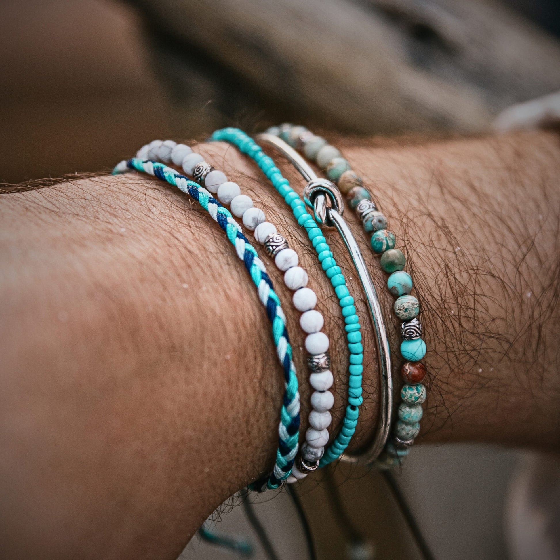 White howlite bracelet stacked with blue and silver bracelets on a man's wrist, showcasing a relaxed coastal style.