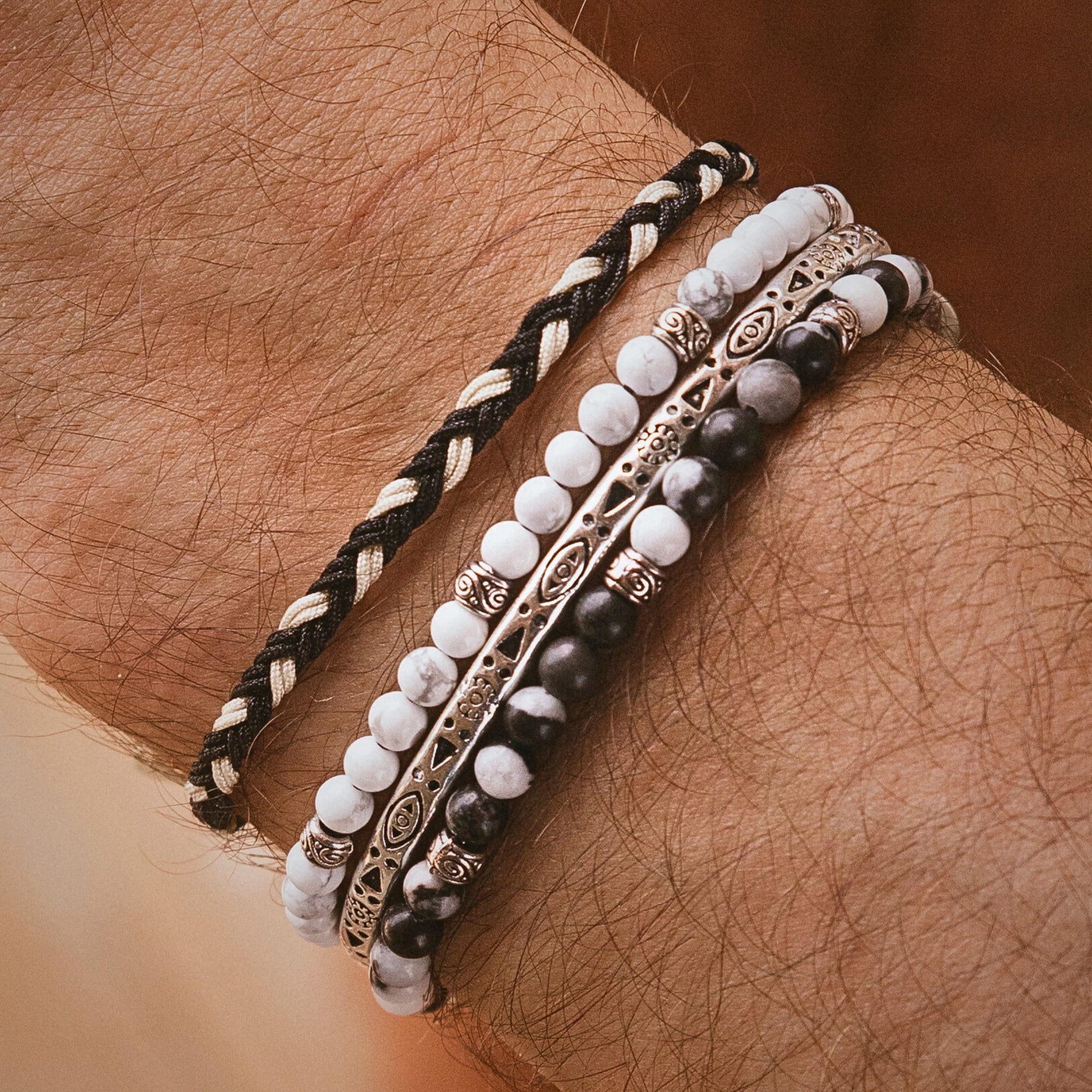 Zebra jasper bracelet styled on wrist with multiple stacked bracelets in black, white, and silver tones for a bold layered look